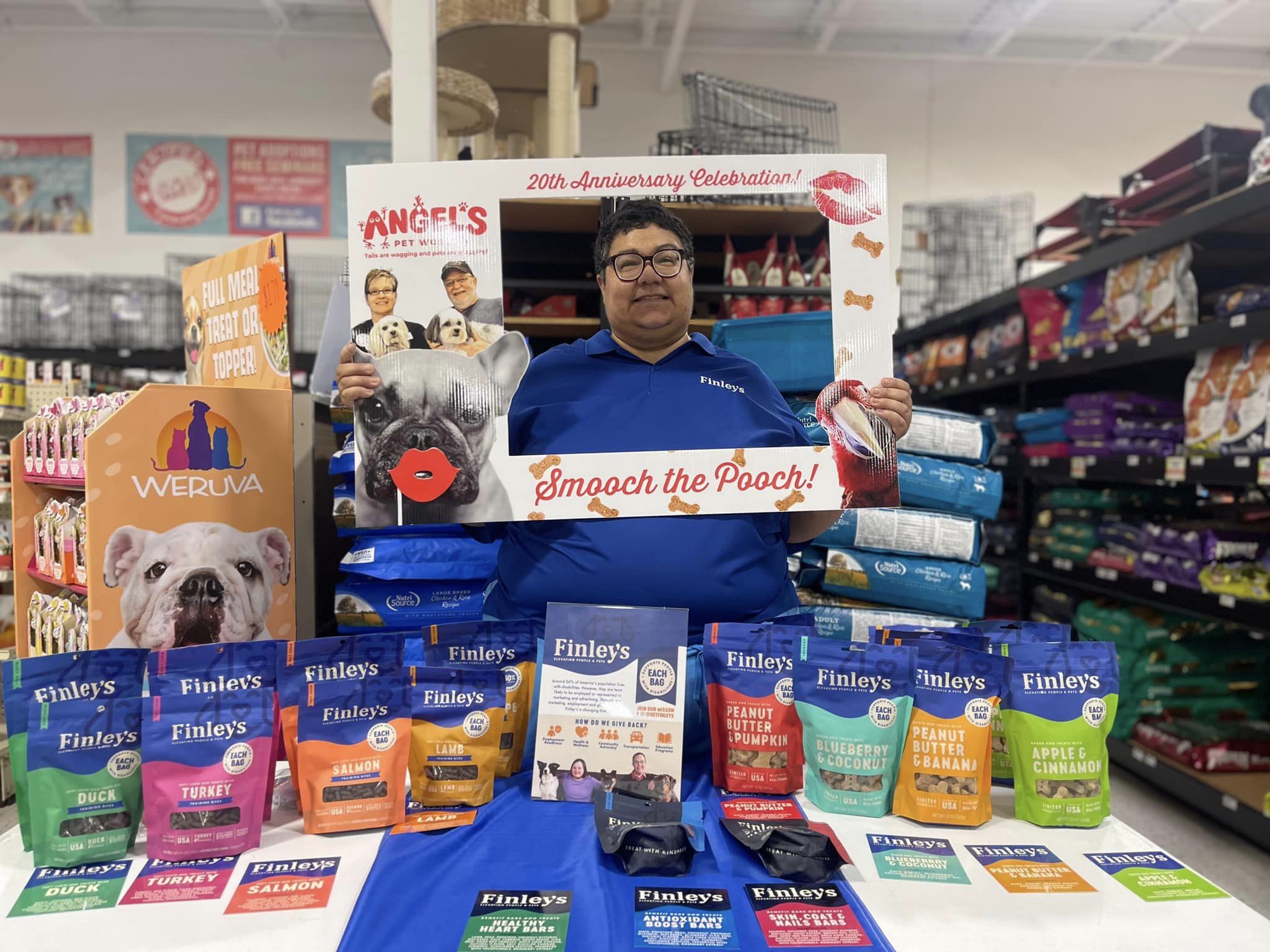 Karen, a Finley's Ambassador is wearing a blue polo standing behind a table of Finley's treats smiling