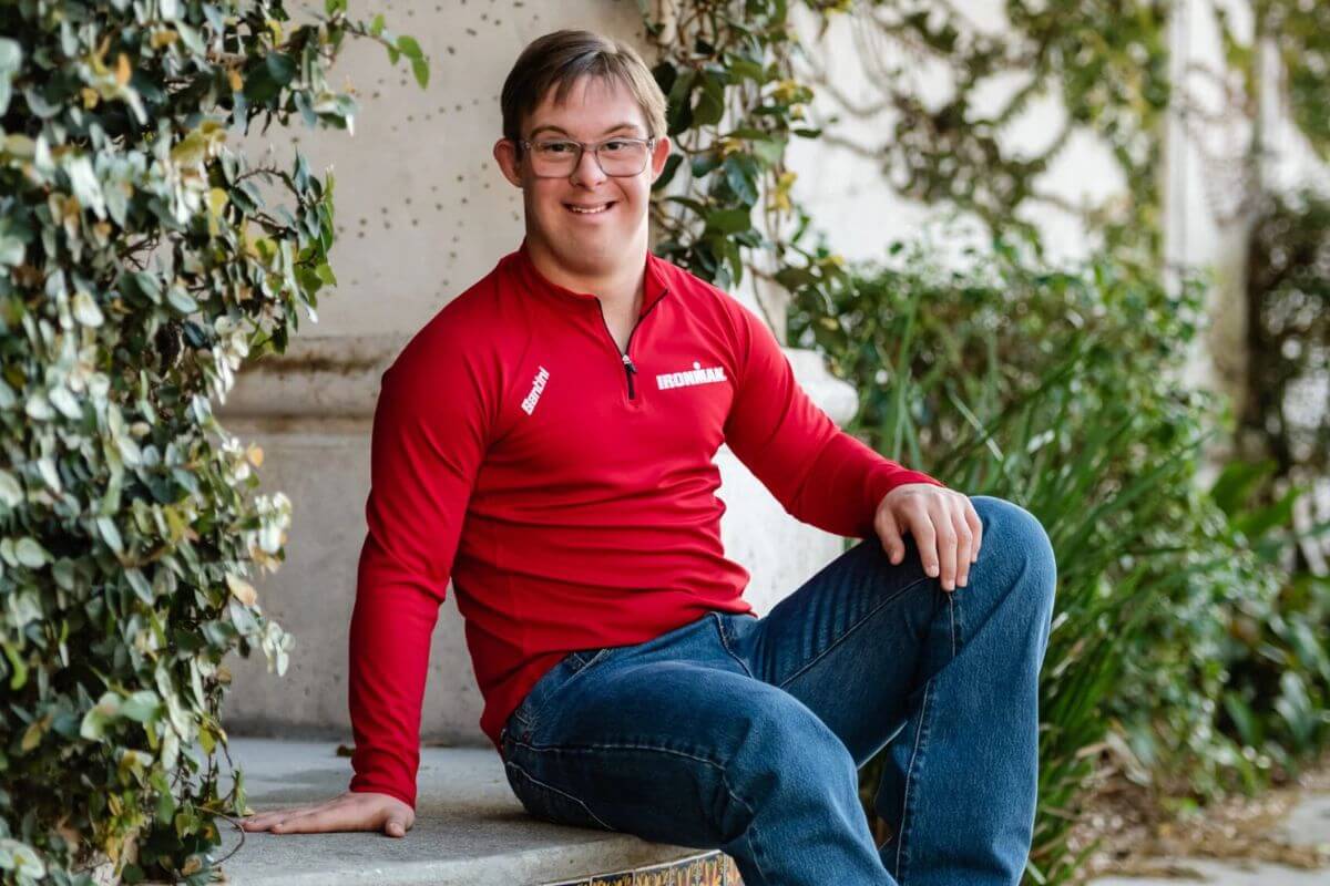 Chris Nikic wearing a red Ironman shirt and sitting outdoors