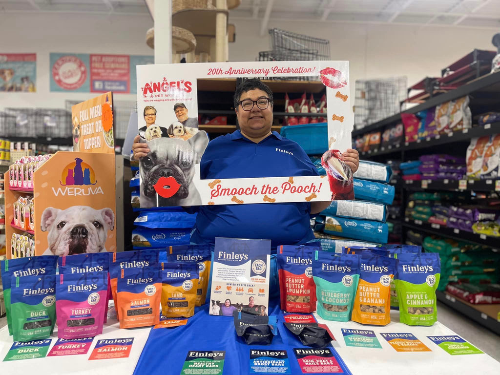 Karen, a Finley's Ambassador is wearing a blue polo standing behind a table of Finley's treats smiling 