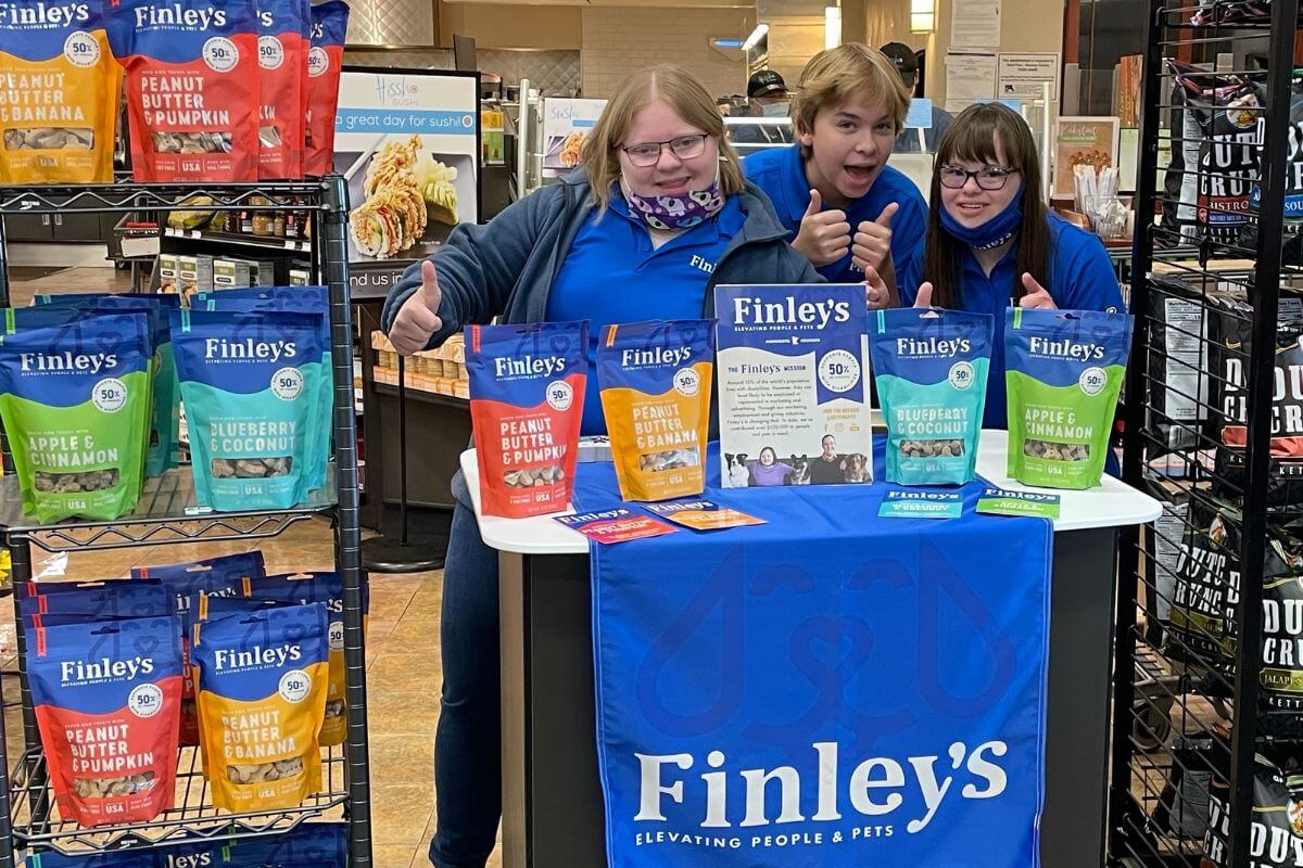 Three people standing behind a table with Finley's pet food bags in a store setting.