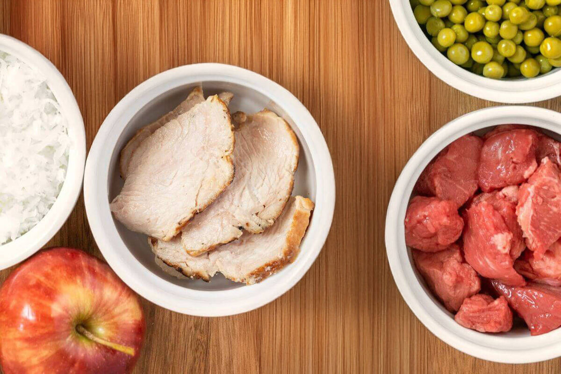 Bowls of sliced meat, peas, and an apple on a wooden surface