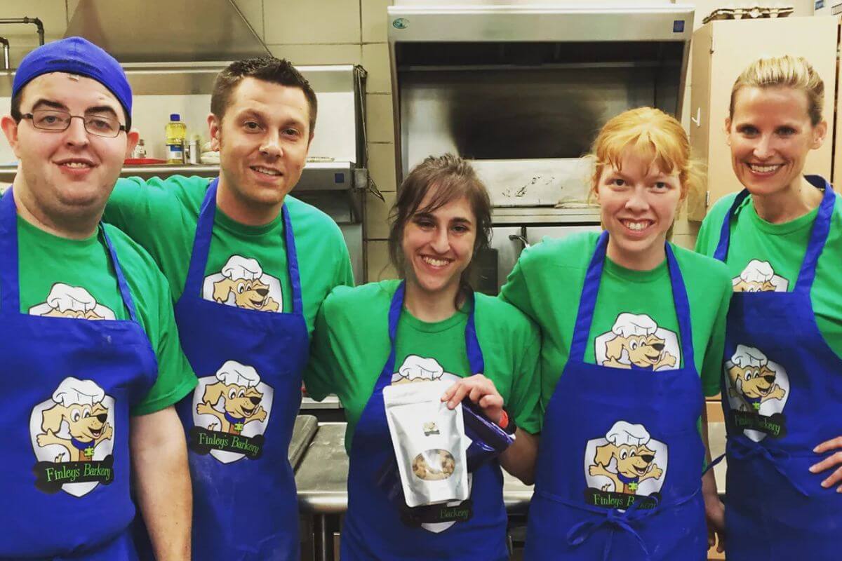 Five people in a kitchen wearing matching Finley's blue aprons and green shirts