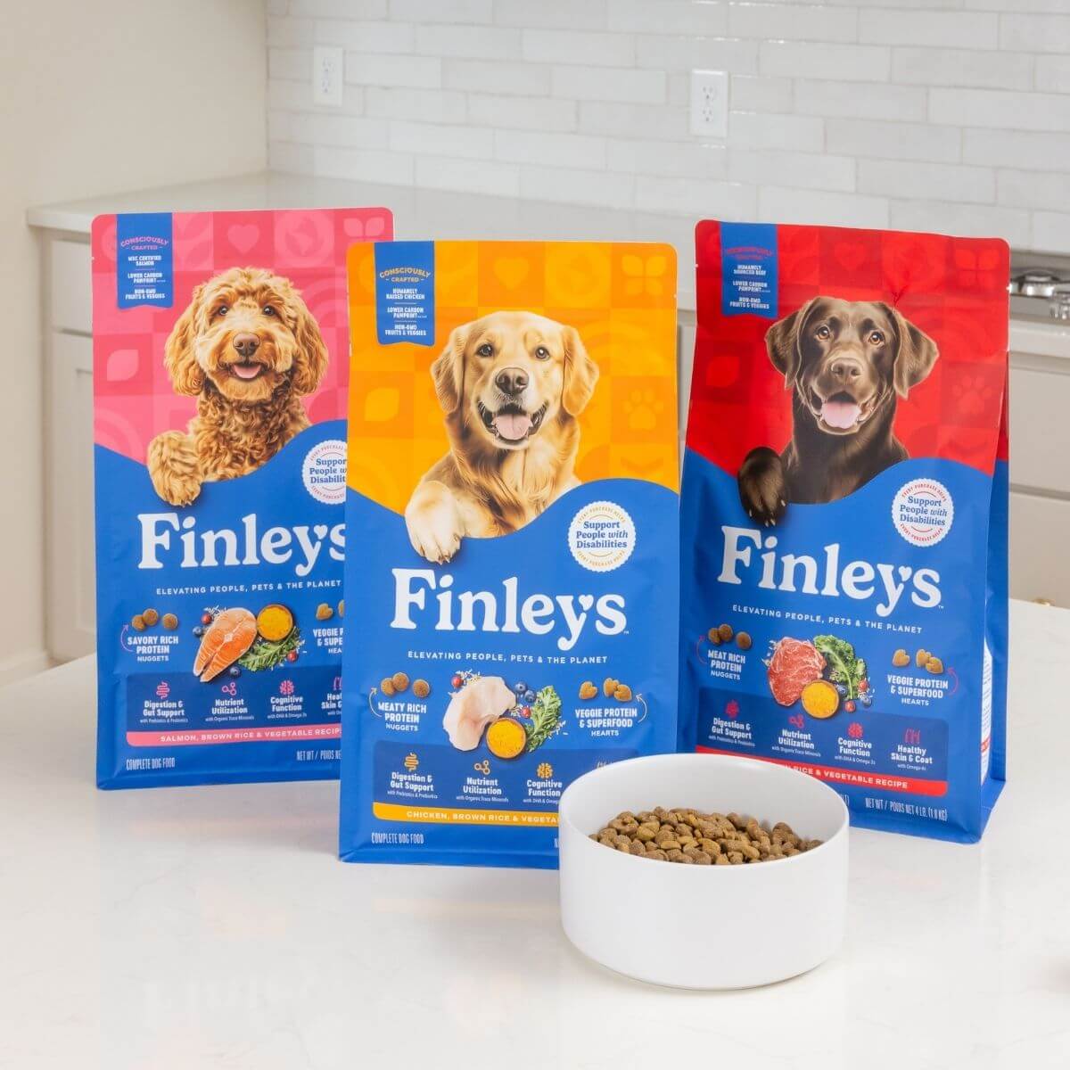 Three packages of Finley's dog food with a bowl of food on a kitchen counter.